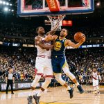 A Golden State Warriors player drives to the basket against a Chicago Bulls defender in a packed arena during a close game